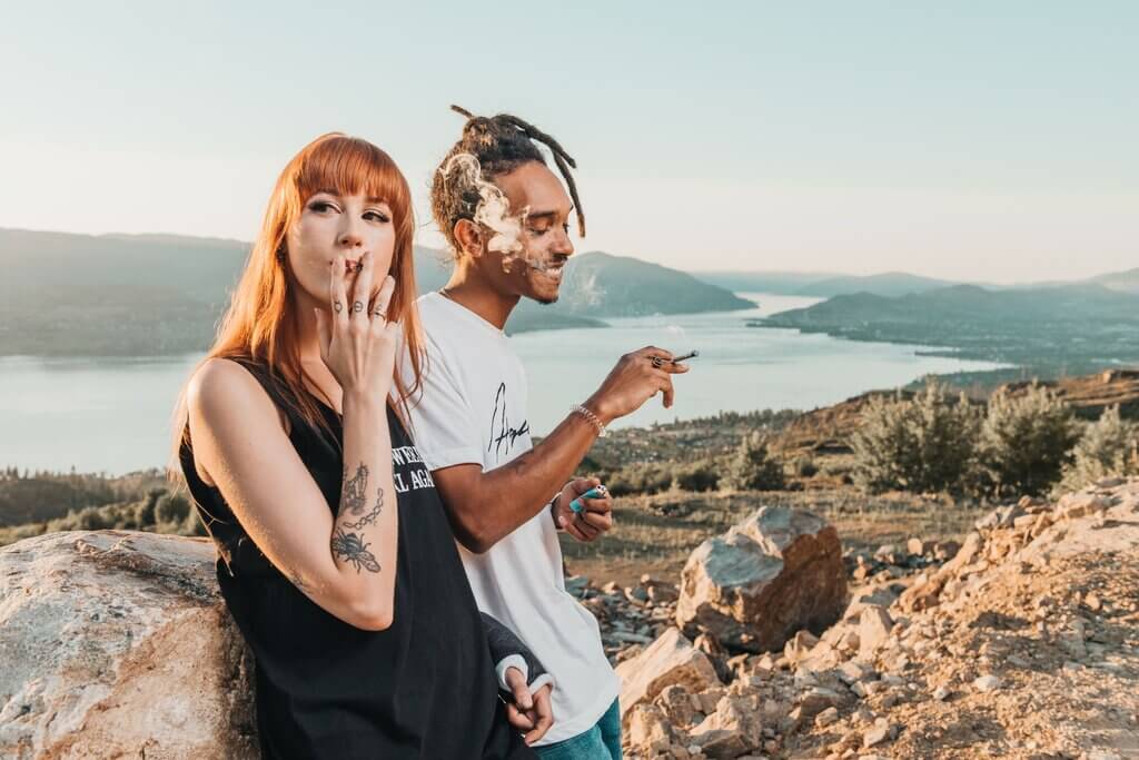 Two friends enjoying cannabis on a hilltop overlooking a BC lake at sunset